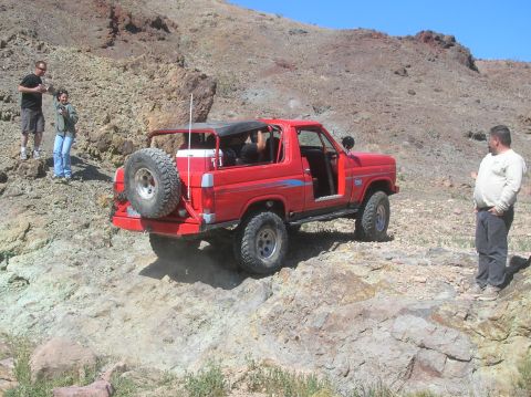 1985 Ford Bronco - A red 1985 Ford Bronco navigates a rocky trail with people watching.
