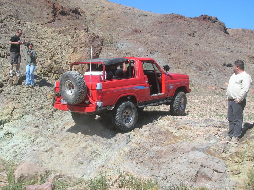 Red 1985 Ford Bronco off-roading on rocky terrain