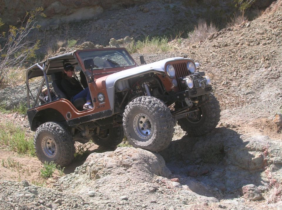 Modified Jeep CJ-7 with roll cage and large tires climbing a rocky hill