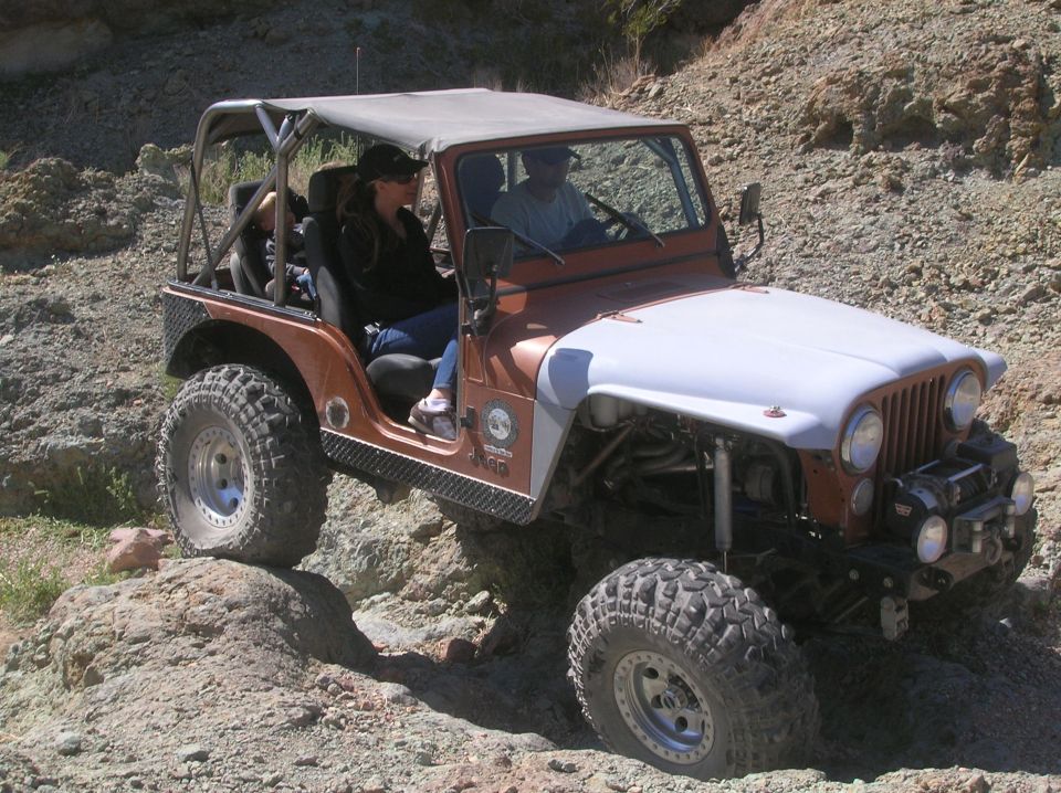 Jeep CJ-7 driving on rocky terrain. Driver and passenger are visible