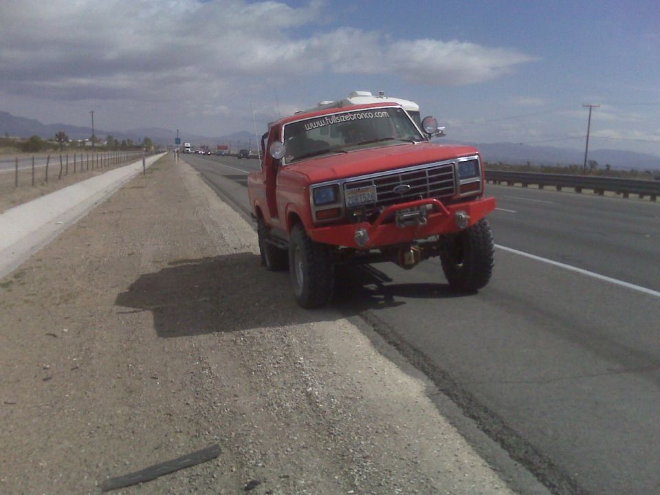 Red Ford Bronco with aftermarket bumper and winch parked on the shoulder of a highway