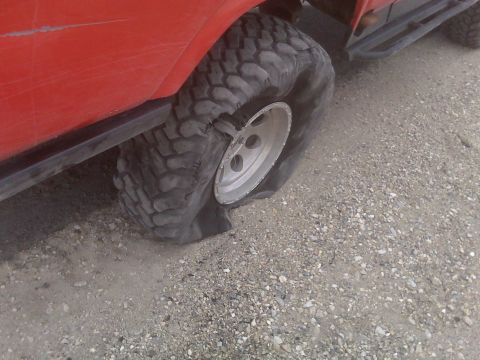 1985 Ford Bronco - A vehicle with a completely flat tire sits on a gravel surface.