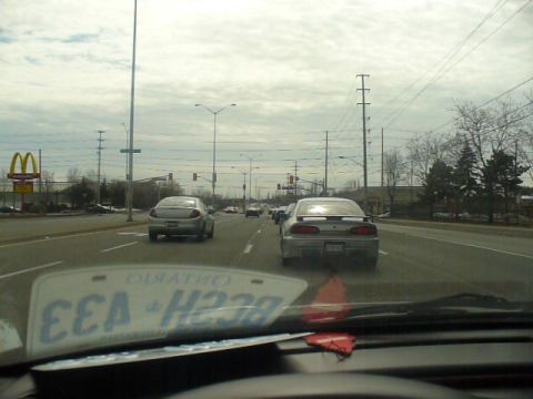 1993 Ford Probe - A silver 1993 Ford Probe is seen from behind on a cloudy day, with other vehicles on the road and a McDonald's in the distance.
