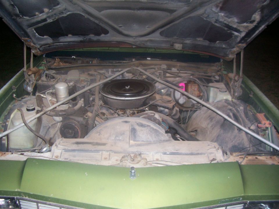 Open hood of green car at night showing dusty V8 engine with round black air cleaner