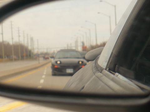 1993 Ford Probe - A black 1993 Ford Probe is seen in the side mirror of another vehicle on a cloudy day.