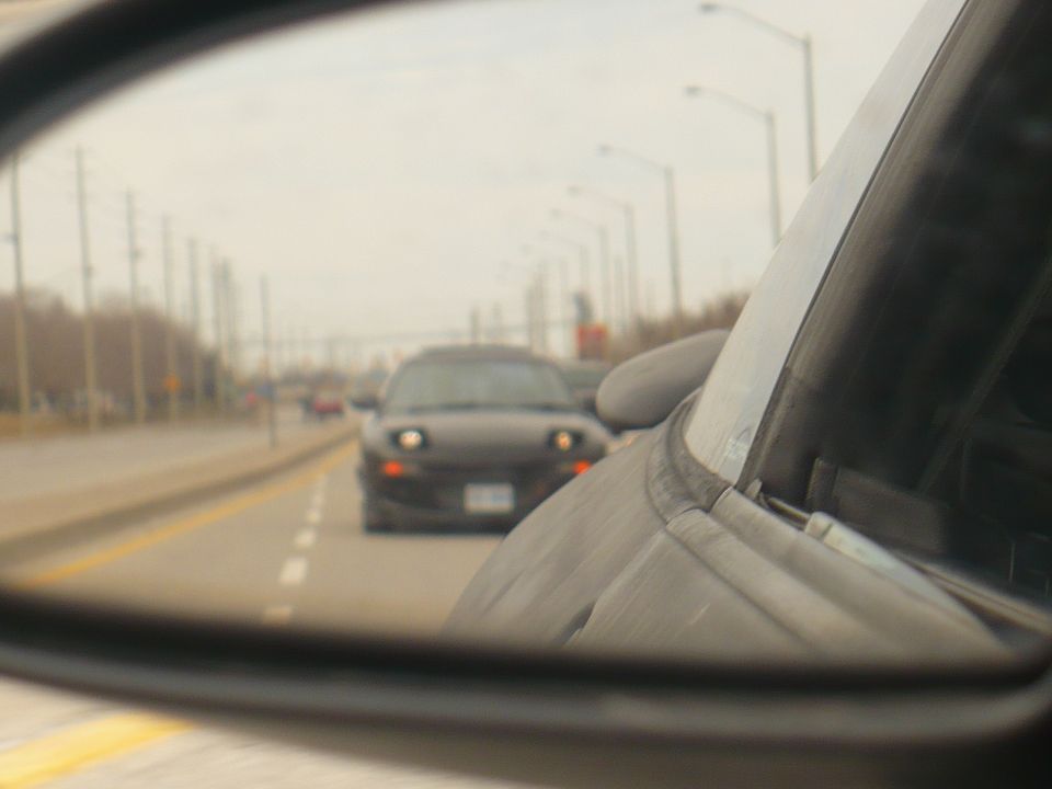 Black 1993 Ford Probe driving on a highway, seen in a side mirror