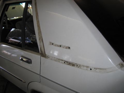 1991 Ford LTD Crown Victoria - The side of a white 1991 Ford Crown Victoria LTD sedan is shown, with visible trim holes and a reflection in the rear window.