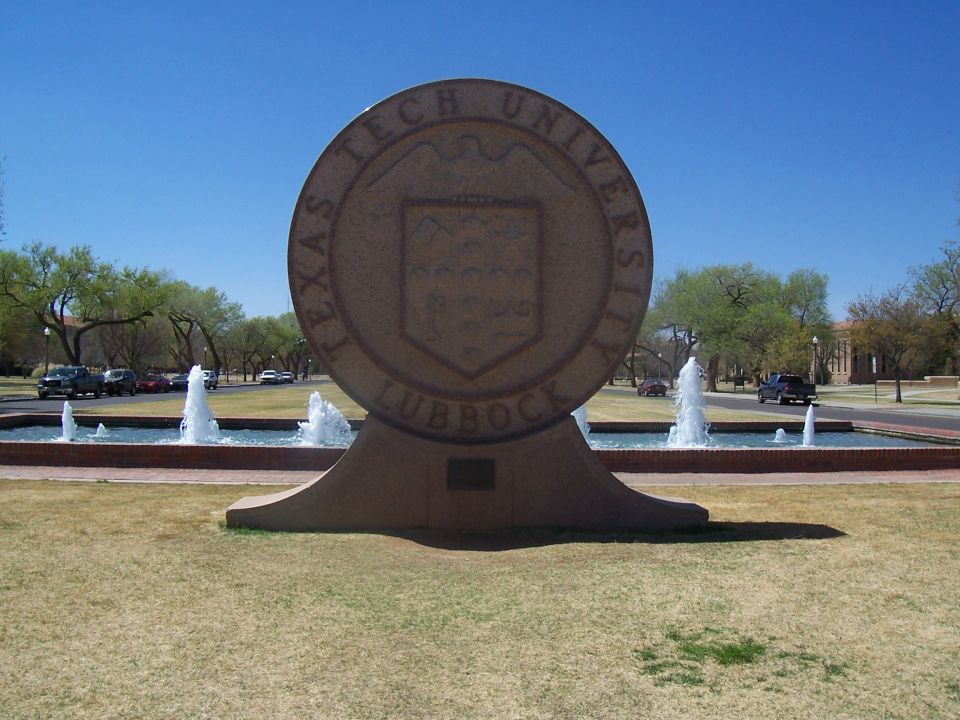Texas Tech University seal sculpture with fountains and several cars parked in the background