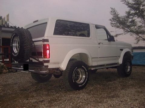 1994 Ford Bronco - This 1994 Ford Bronco is seen from the rear, parked on a gravel surface with trees and water in the background.