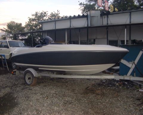 1994 Ford Bronco - A boat is parked on a trailer next to a white SUV, with a building in the background.