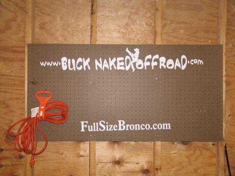 1995 Ford Bronco - A sign with off-road website addresses is mounted on a pegboard wall. An orange extension cord is coiled to the left.