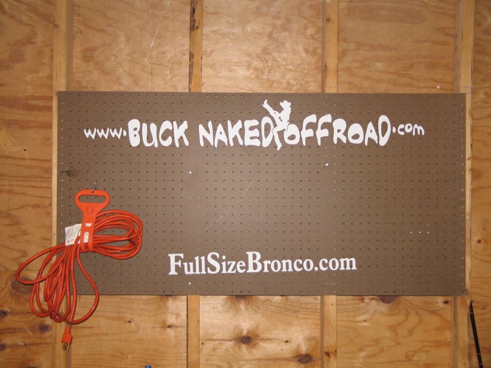 Pegboard with white text: www.BUCKNAKEDOFFROAD.com and FullSizeBronco.com. Orange extension cord hangs on left