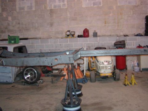 1991 Ford Bronco - The bare frame of a vehicle is elevated on jack stands in a workshop setting.