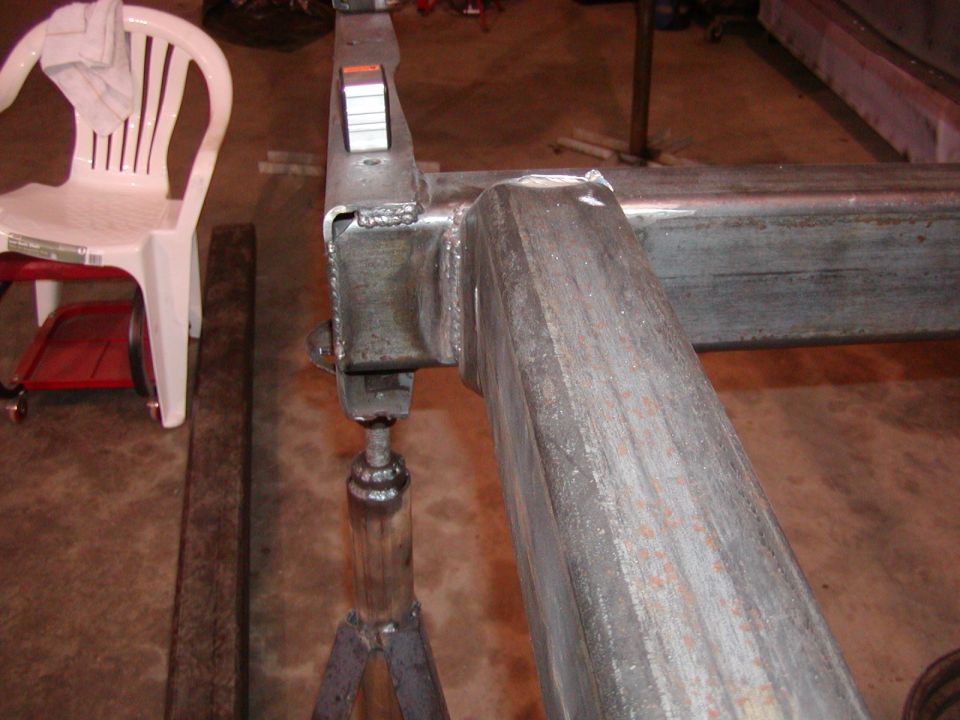 Welded steel frame section on jack stands, white plastic chair in background