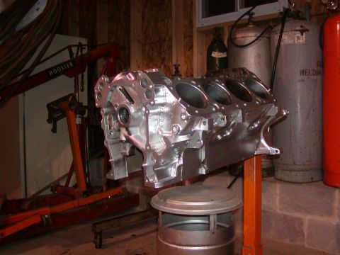 1991 Ford Bronco - A bare engine block sits on an orange stand in a workshop, with welding tanks and an engine hoist nearby.