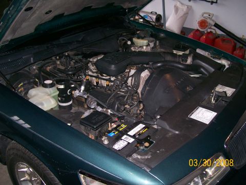 1995 Mercury Grand Marquis - The engine bay of a 1995 Mercury Grand Marquis is shown with the hood open, revealing the engine components and battery.