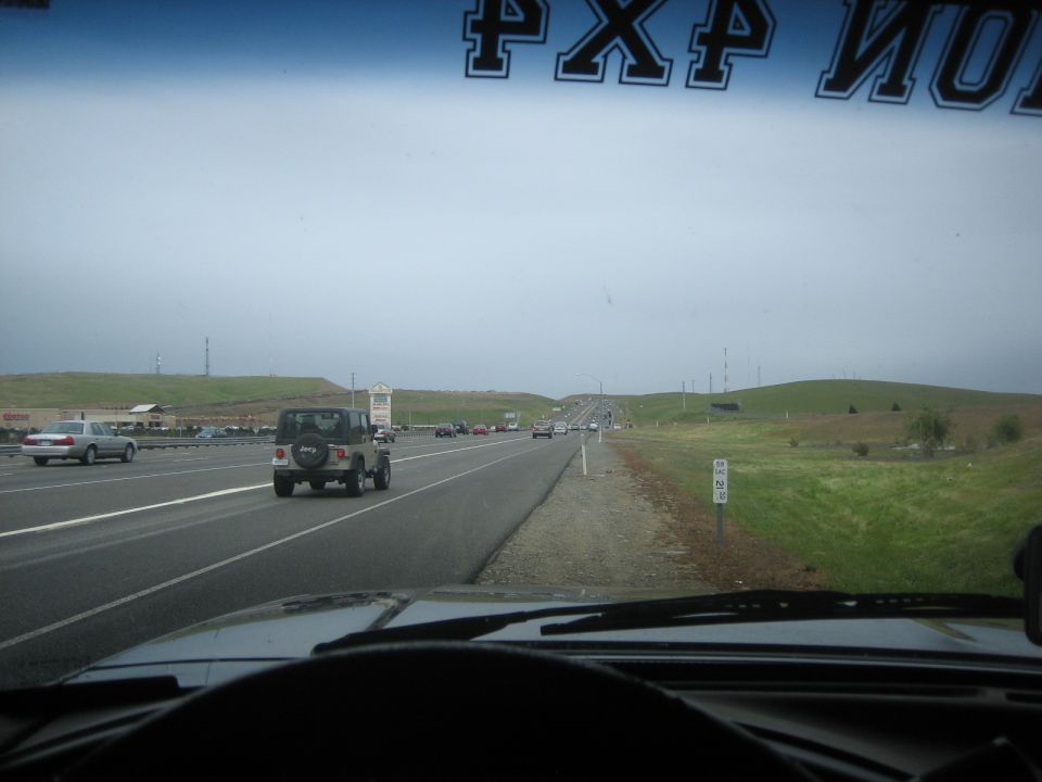 Jeep Wrangler driving on highway, rear view, spare tire on back
