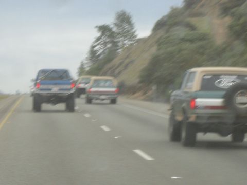 1995 Ford Bronco - A 1995 Ford Bronco is seen from the rear, driving on a highway alongside other vehicles.