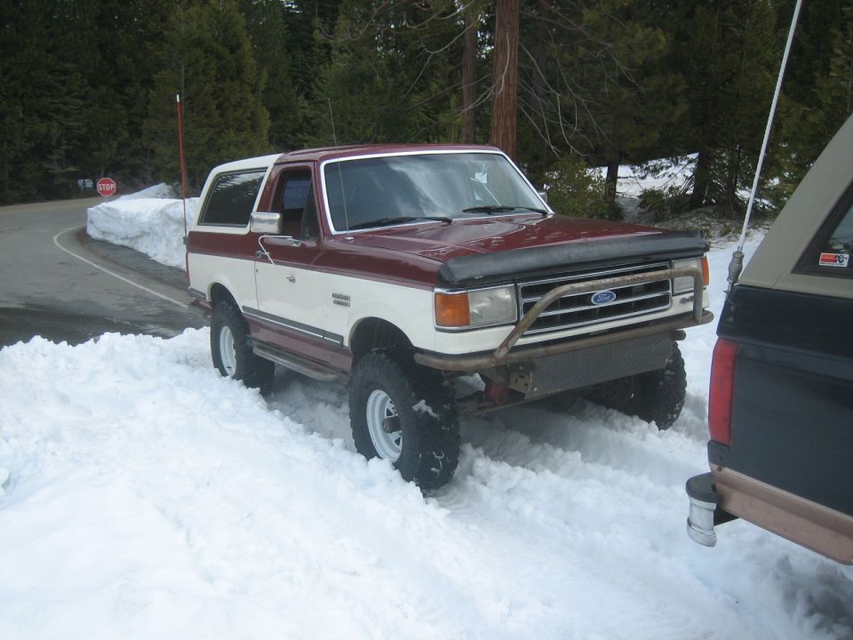 Maroon and white Ford Bronco with a brush guard stuck in snow
