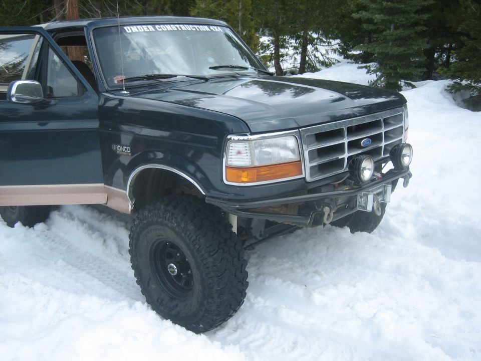 Dark green Ford Bronco with tan lower trim, lifted suspension, and aftermarket bumper in snow
