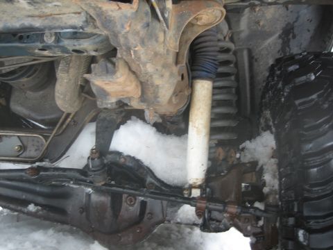 1995 Ford Bronco - Undercarriage view of a vehicle's suspension system and tire, partially covered in snow.
