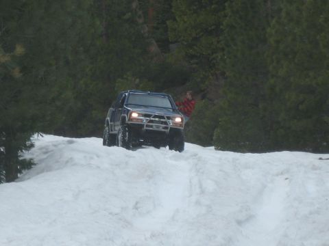 1995 Ford Bronco - A 1995 Ford Bronco navigates a snowy incline, its off-road capabilities with a prominent aftermarket bumper.