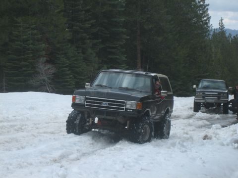 1995 Ford Bronco - A black Ford Bronco navigates a snowy terrain with another vehicle visible in the background.