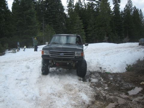 1995 Ford Bronco - A black Ford truck with a lifted suspension navigates a snowy, muddy terrain.