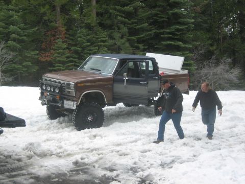 1995 Ford Bronco - Lifted pickup truck in snowy conditions with two men walking around it.