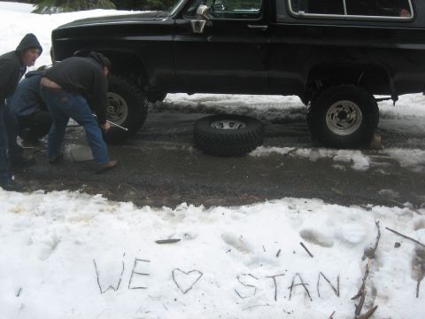 1995 Ford Bronco - People work on a black SUV with a flat tire in a snowy environment, with 'WE LOVE STAN' written in the snow.