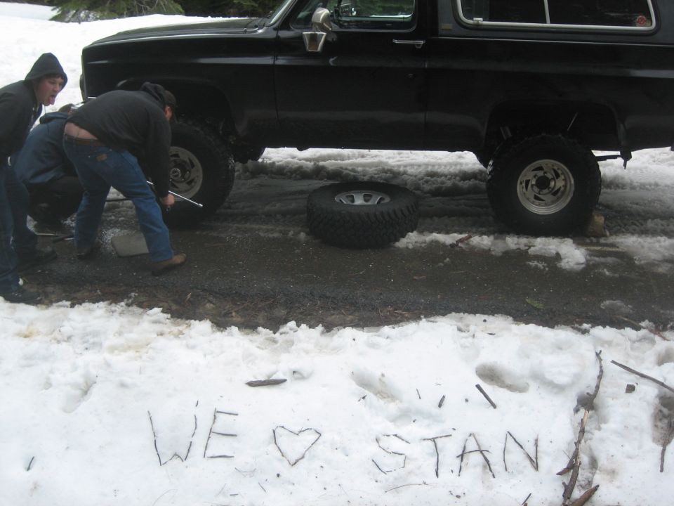 Black SUV with lifted suspension and off-road tires, a flat tire on the ground, people working on it in the snow