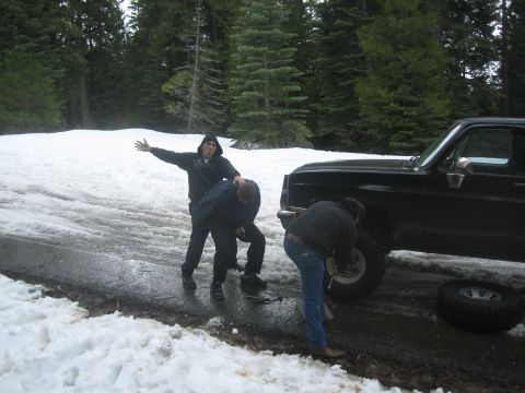 1995 Ford Bronco - A group of people work to change a tire on a black 1995 Ford Bronco in a snowy, wooded area.