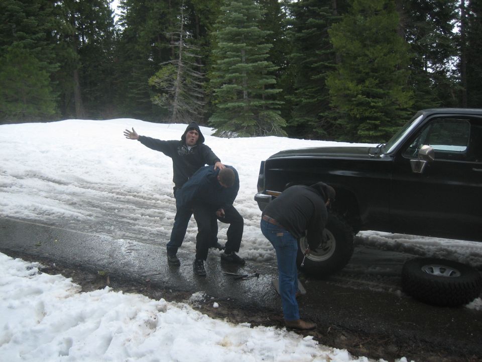 Black 1995 Ford Bronco side view, people changing tire in snow
