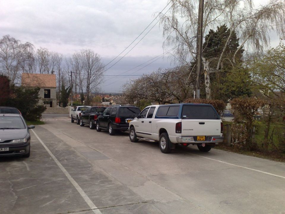 Several trucks and SUVs parked in a row, with a white pickup truck with a camper shell in the foreground