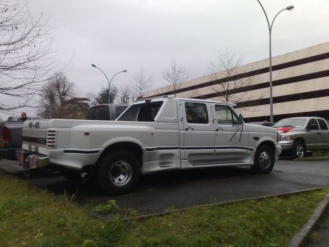 1991 Ford Crown Victoria - A white crew cab dually pickup truck with a custom body kit is parked next to other vehicles.