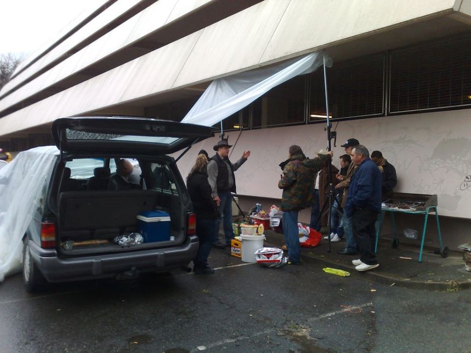 Rear view of an open van with people gathered around it and a grill