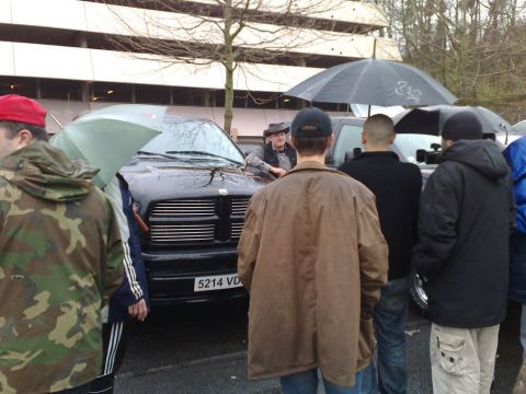 1991 Ford Crown Victoria - A group of people gather around a black Dodge Ram pickup truck on a rainy day, with umbrellas providing shelter.