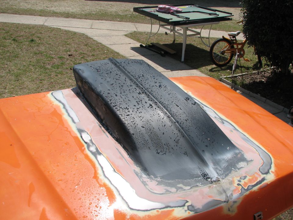 Gray primer-coated cowl induction hood scoop bonded onto an orange truck hood