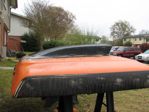 1979 Ford Bronco - Low side view of an orange hood resting on black sawhorses in a yard, with a black cowl scoop grafted on and the front and rear edges sande…