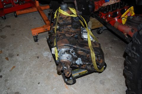 1994 Ford Bronco - A transmission unit is shown on a dolly, secured with yellow straps, with other vehicle parts in the background.