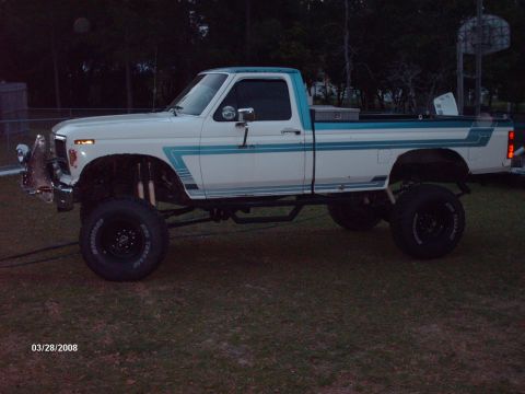1982 Ford F-100 - This lifted pickup truck has a distinctive blue stripe graphic along its side and a toolbox mounted in the bed.