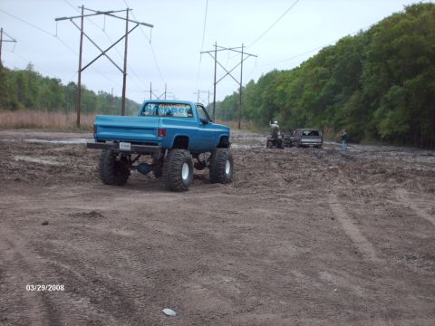 1982 Ford F-100 - Modified pickup truck with oversized tires parked in a muddy outdoor area with other vehicles.