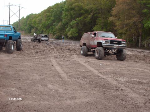 1982 Ford F-100 - Several off-road vehicles are stuck in a muddy area with trees in the background.