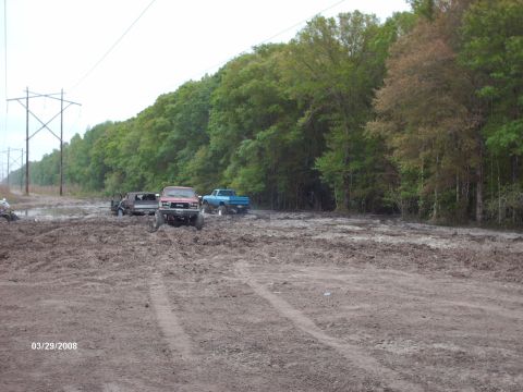 1982 Ford F-100 - Several trucks are stuck in a muddy area with trees and power lines visible.