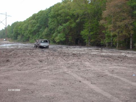 1982 Ford F-100 - A vehicle navigates a muddy terrain, with trees lining the background and a date stamp visible.
