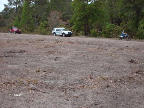1982 Ford F-100 - A Sheriff's SUV and a red Jeep are visible in a dirt lot with trees in the background.