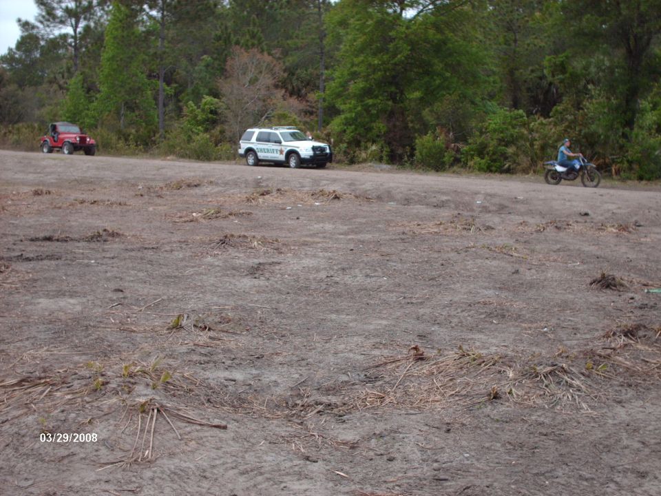 Sheriff SUV and red Jeep parked on dirt lot