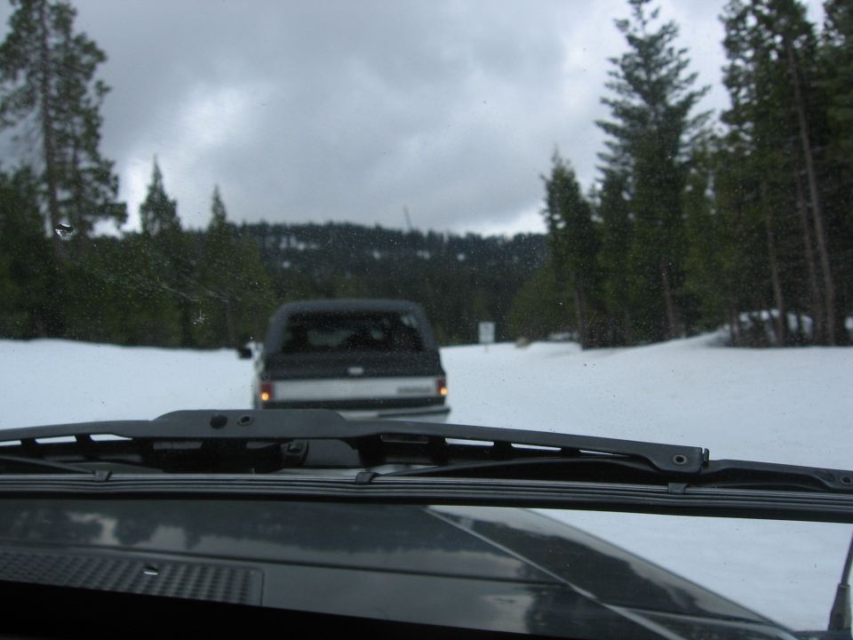 Driving behind a pickup truck on a snowy road with pine trees