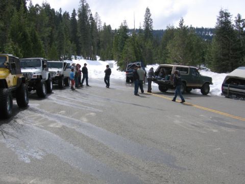 1989 Ford Bronco - Several off-road vehicles and people gathered in a snowy, forested location.
