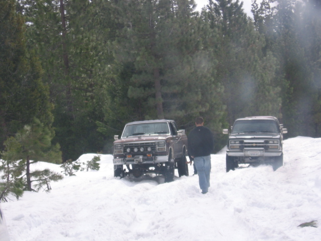 Brown pickup truck with auxiliary lights in snow, followed by a dark SUV